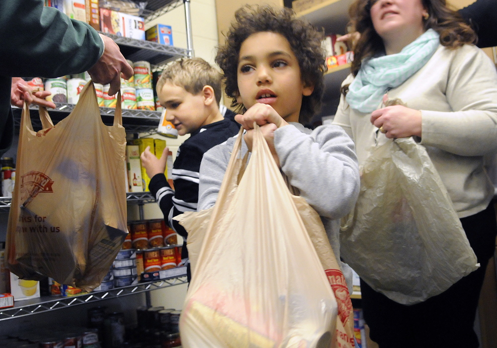 Chelsea School students Jaydyn Lachzik, right, fills a bag of groceries Thursday with fellow student Mitchell Dusoe at the school’s food bank. Students in need of additional food are welcome to bring the bags home with them. The children filled several bags for classmates.