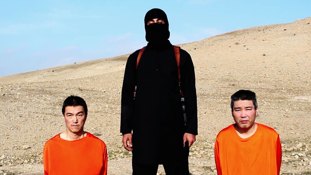 This image taken from an online video released by the Islamic State shows the group threatening two Japanese hostages who were later killed. One of the men posing with hostages in the videos, nicknamed “Jihadi John,” has been identified as a man known to the British intelligence services since at least 2009.