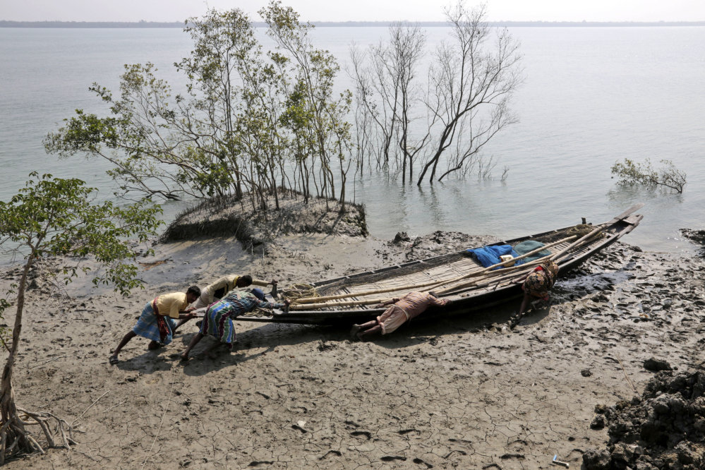 In this Feb. 1, 2015, photo, villagers help fishermen  push their boat to the water at Satyanarayanpur village in the Sundarbans, India.