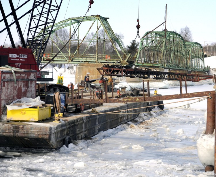 Reed & Reed contractors move equipment Monday between a pier on the Kennebec River in Dresden and a raft with a crane used to raze the old bridge that spanned the river between Richmond and Dresden. Reed & Reed is dismantling the existing five-span steel truss bridge and bridge piers that supported it.