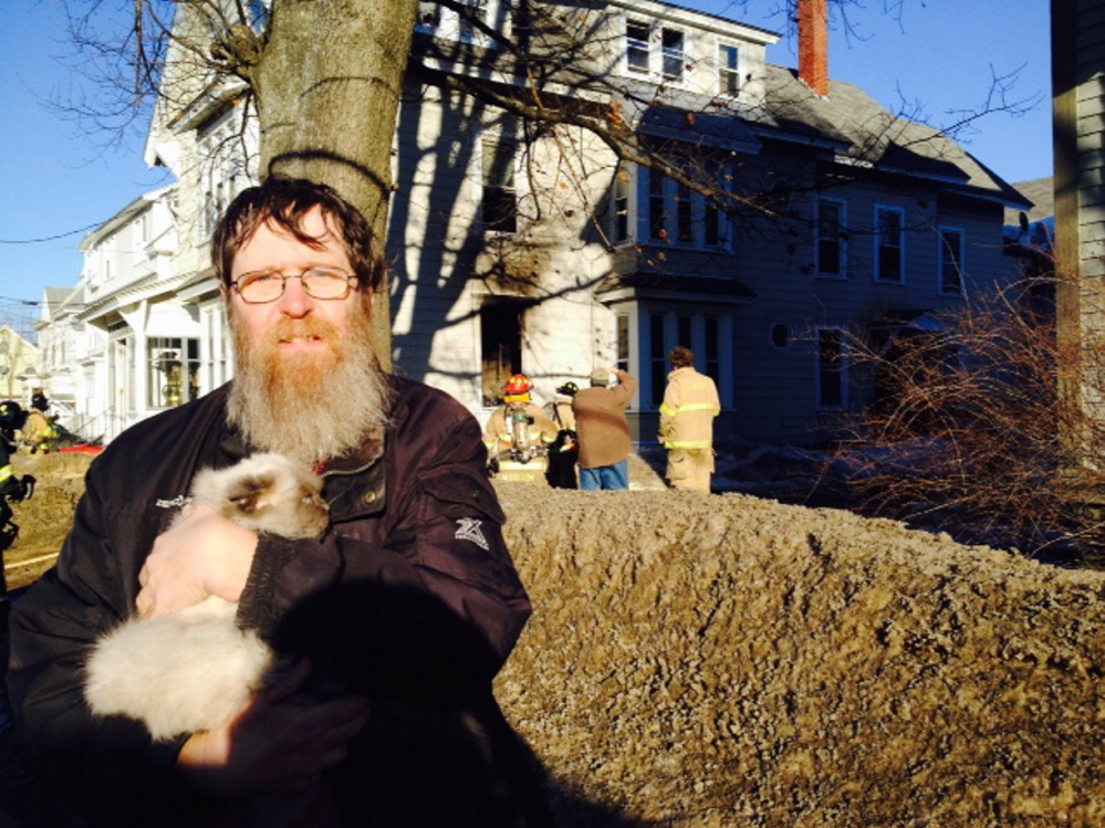 Peter Beach, a resident of 58 Silver St. in Waterville was among the residents forced to leave the building when fire broke out Friday afternoon. Beach left with his cat, China, while firefighters went to work in the building, in the background.