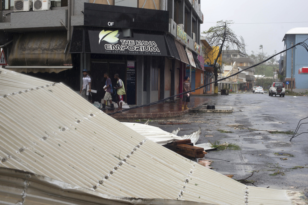 People walk past debris scattered on a street in Port Vila, Vanuatu, on Saturday in the aftermath of Cyclone Pam. Winds from the extremely powerful cyclone that blew through the Pacific’s Vanuatu archipelago are beginning to subside, revealing widespread destruction.