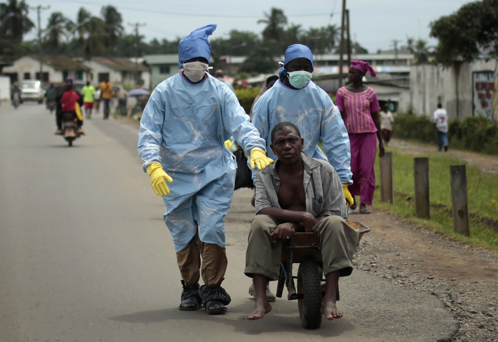 In this file photo taken on Sunday Sept. 28, 2014, residents of the St. Paul Bridge neighborhood wearing personal protective equipment take a man suspected of carrying the Ebola virus to the Island Clinic in Monrovia, Liberia.