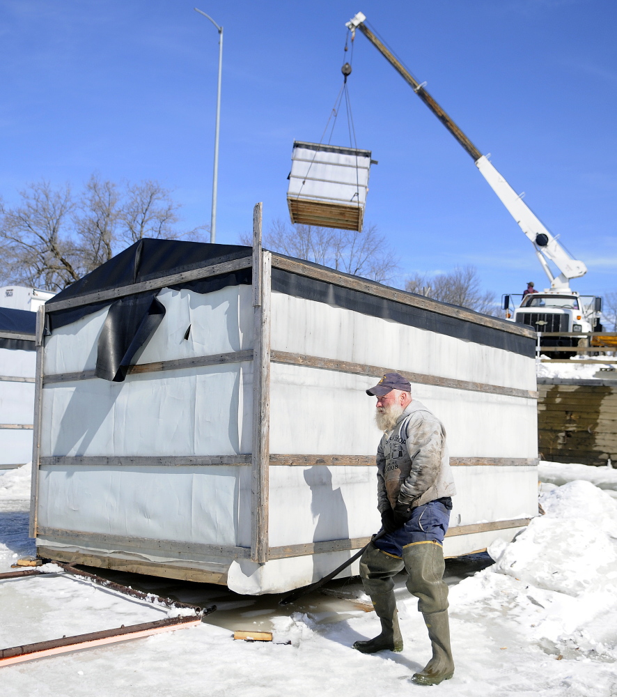 Jimmy Worthing levers a smelt camp off the ice Monday on the Kennebec River in Randolph as another shack is hoisted to shore. Worthing’s Smelt Camps removed 20 of the shacks from the ice but plans to keep several available for fishermen.