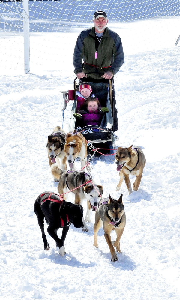 Musher Kevin Quist, of Heywood Kennel in Augusta, and his team of dogs take Cornville Regional Charter School students Maddy Thorndike, left, and Isabella Mullen for a ride at the school on Monday. “That was cool,” both girls shouted at the end of the ride.