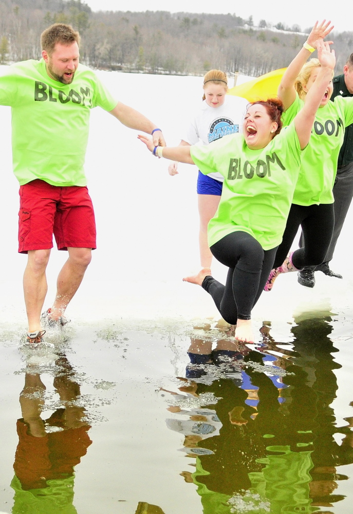 Green-shirted Team Bloom members Corey Rubchinuk, left, Kayla Diplock and Kim Stoneton leap into Marancook Lake during last year’s Ice Out Plunge at the town beach in Winthrop.