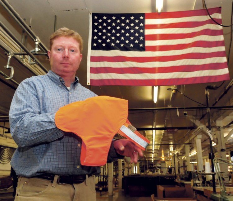 Bill Swain, owner of Maine Stitching Specialties in Skowhegan, holds an L.L. Bean No Fly Zone dog vest beside and American flag made at the Skowhegan company on Wednesday.