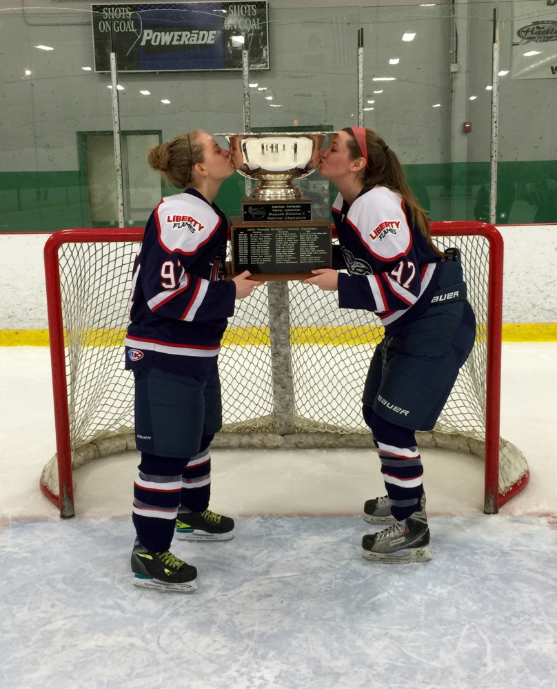 Winslow’s Sarah Fowler, right, kisses the ACHA Division I championship trophy along with Liberty University teammate Courtney Gilmour. The Flames defeated Miami (Ohio) 4-1 on March 8 to win the title.