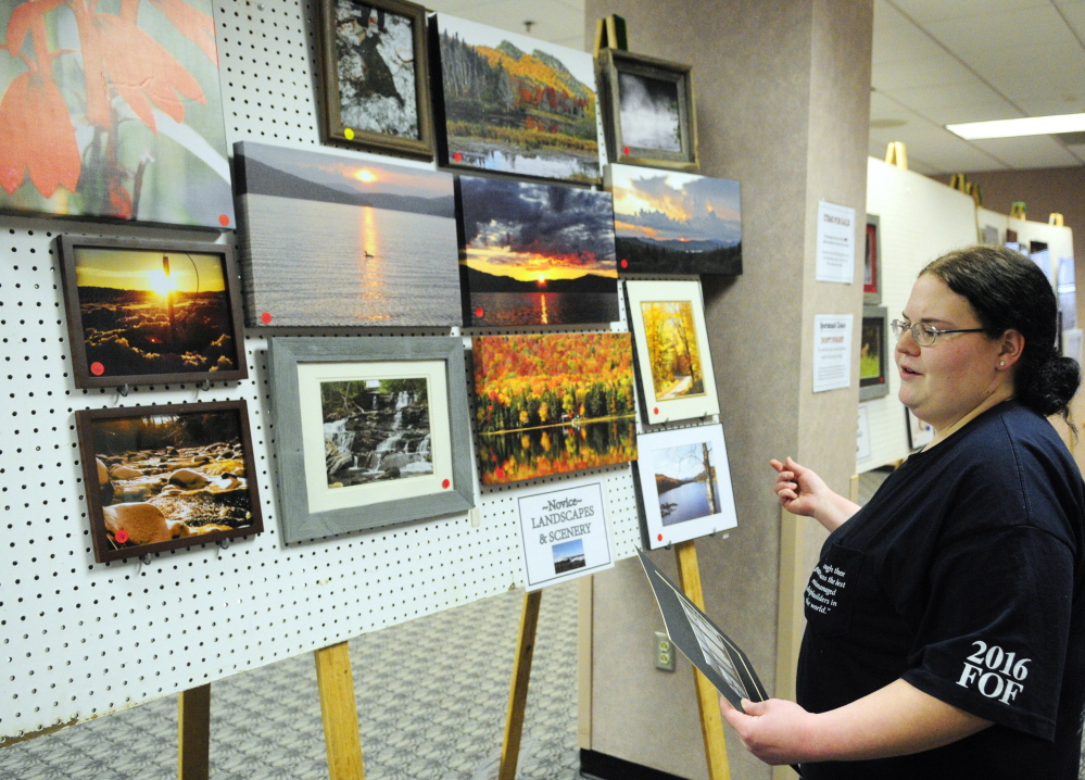 Becky Pass looks for a space to hang another landscape photo as she helps set up the art and woodcarving show Thursday, the day before the opening of the Maine Sportsman’s Show at the Augusta Civic Center.