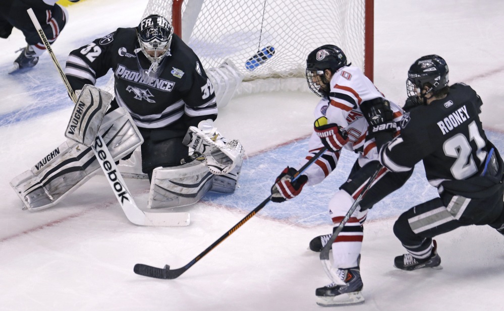 Providence goalie and South Portland native Jon Gillies, left, follows the puck as Omaha forward Tyler Vesel, center, tries for a back-hander during the first period Thursday of their semifinal game at the NCAA Frozen Four in Boston. At right is Providence forward Kevin Rooney.