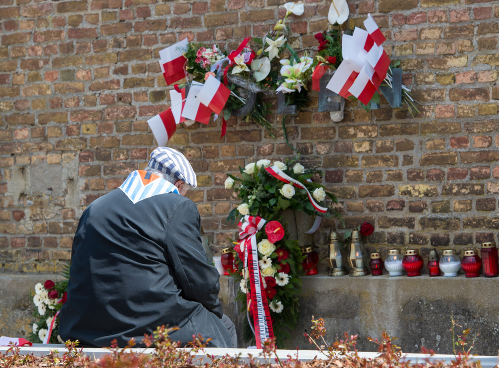 A Nazi concentration survivor from Poland sits at the ‘Wall of Nations’ in front of the word ‘Polen’ (Poland), adorned with flowers and flags, at the Ravensbrueck concentration camp memorial site during the memorial  ceremonies marking  the 70th anniversary of the camp’s liberation in Fuerstenberg, Germany, on Sunday.
