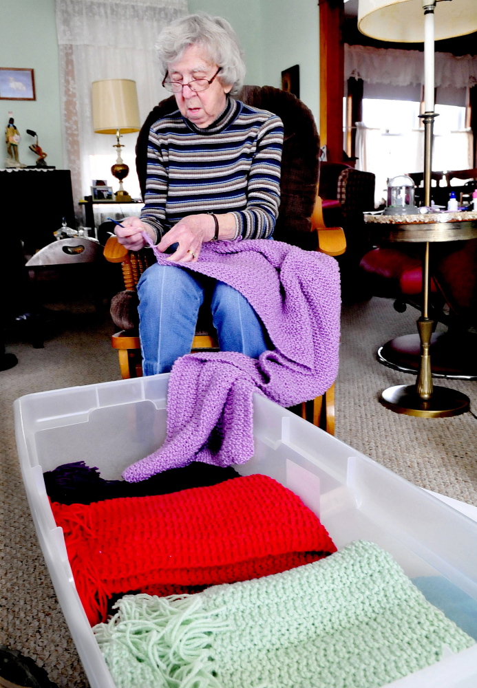 Sitting behind a container full of finished shawls at her home in Waterville, Lillian Tulley, 91, works on her latest shawl that she makes for comfort and warmth of patients dealing with cancer. Tulley said she has made 91 in the last three years.