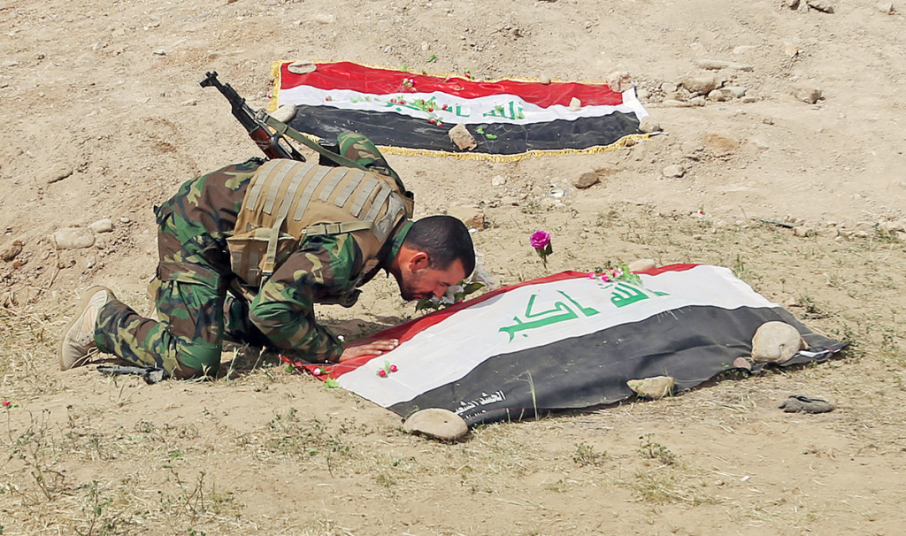 A Shiite militiaman kisses a grave on Friday at the site where Islamic State militants are believed to have buried  hundreds of Iraqi soldiers. The Associated Press