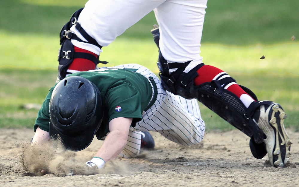 Winthrop High School’s Adam Hachey dives between the legs of Hall-Dale High School catcher Sam Moulton to arrive safely at home during a Mountain Valley Conference game Monday in Farmingdale.