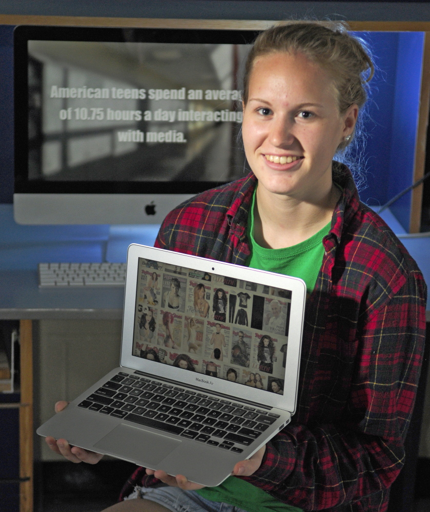 Gardiner Area High School senior Emma Hickey poses Thursday in her broadcast journalism class with shots from her award-winning short film, “Drop the Gender Mask,” on the screens.