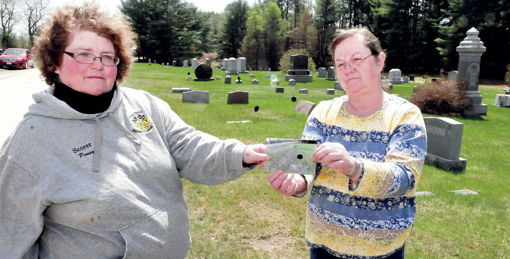 Penny Picard-Sampson, left, a member of the Unity Board of Selectmen and the Cemetery Committee, and committee member Lynn Warman hold a recent photograph of a Pond Cemetery grave covered with gravel and dust from nearby Kanokolus Road. The town converted the road from asphalt to gravel two years ago, and since then grave sites have been littered with rocks and dust. A group of citizens is asking the town to repave the road.