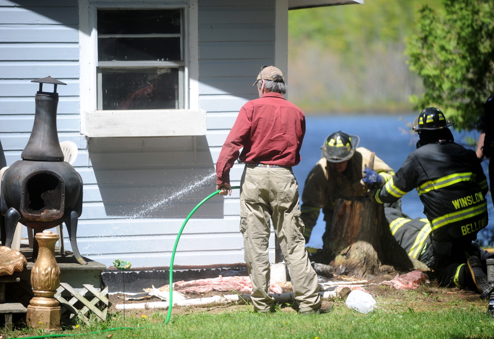 Bob Davis uses his garden hose Saturday to subdue a fire under his camp on Catfish Corner Road in Winslow. A wood stove ember caused the fire, according to the Winslow Fire Department.