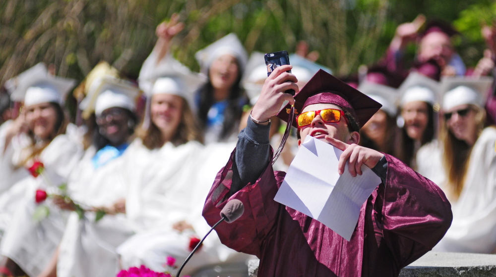 Standing at the lectern, Kevin Rodgers takes a selfie with his classmates before giving the senior address Saturday at the Kents Hill School graduation ceremony in Readfield.