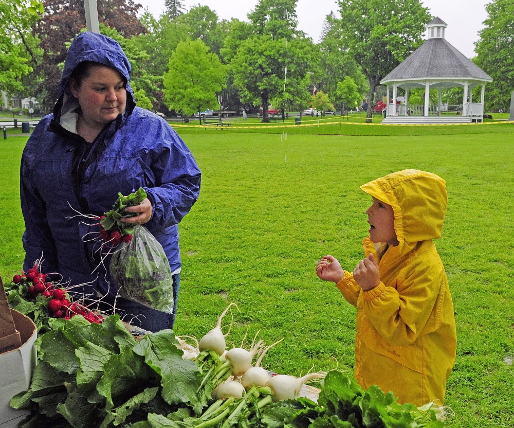 Christine Leavitt, left, and Rylee Lefebvre buy vegetables on a rainy June 4, 2014, in front of the gazebo during the farmers market on the Gardiner Common. Gardiner’s market is one of more than 30 farmers markets in Maine that will receive grant money over the next three years to encourage people receiving food stamp benefits to buy more fruit and vegetables.