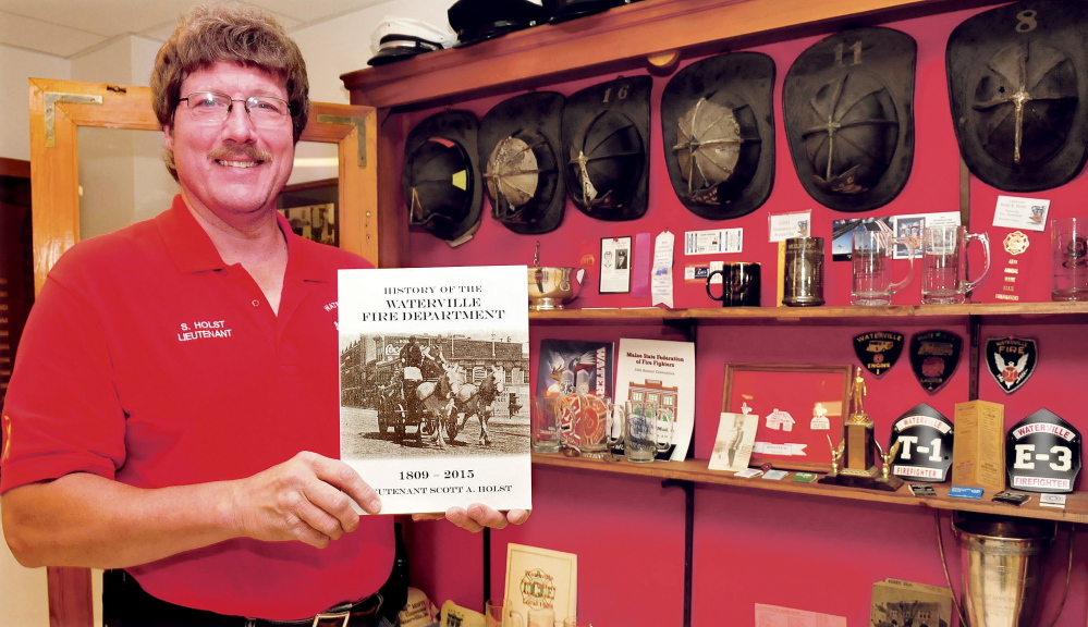 Firefighter Lt. Scott Holst holds a copy of his book “The History of the Waterville Fire Department, 1809-2015” on Tuesday beside a case filled with department memorabilia at the fire station.