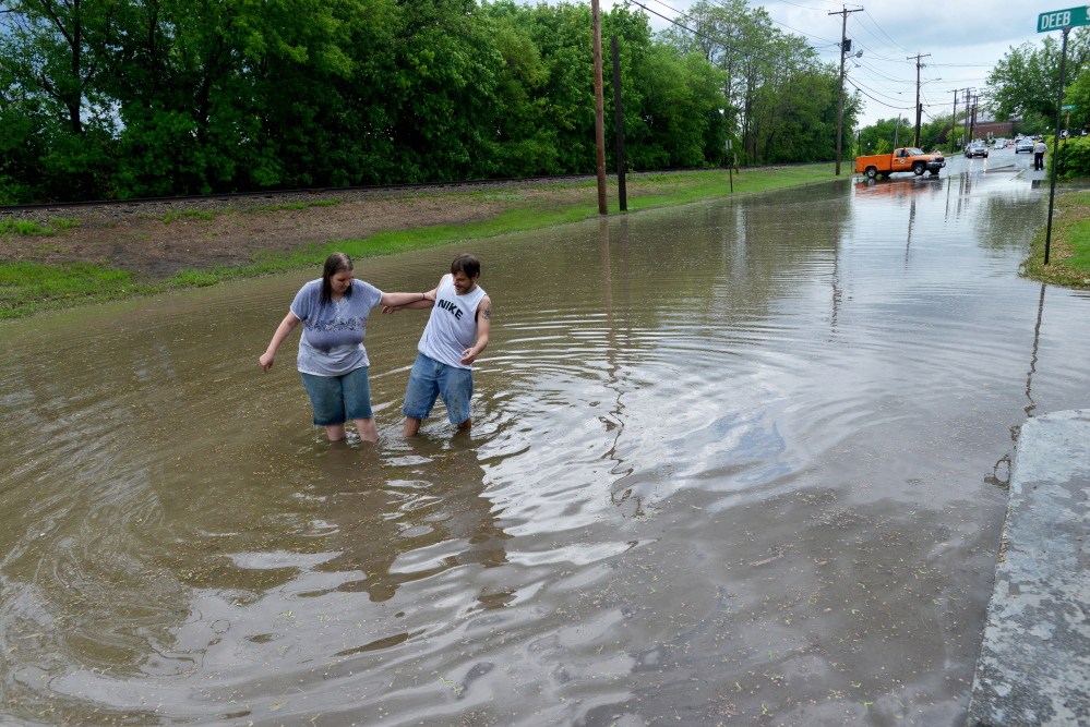 Danielle Crutcher and Joseph Morissette walk through the flood waters on Front Street in Waterville on Thursday.