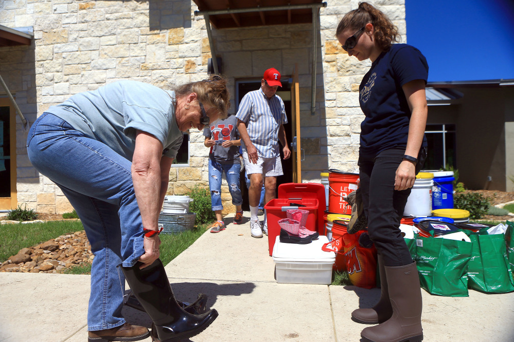 Volunteers Diana Harlien, left, and Rebecca Rippy from Austin try on boots to prepare to help residents clean their homes Friday at the Cypress Creek Church in Wimberley, Texas.