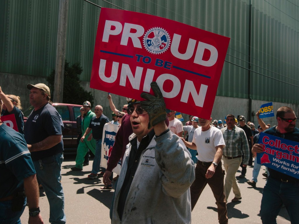 Bath Iron Works pipe fitter Dan Ouellette of Freeport holds a union sign while marching in protest of a proposal by the company to reclassify workers' jobs in Bath on Thursday.