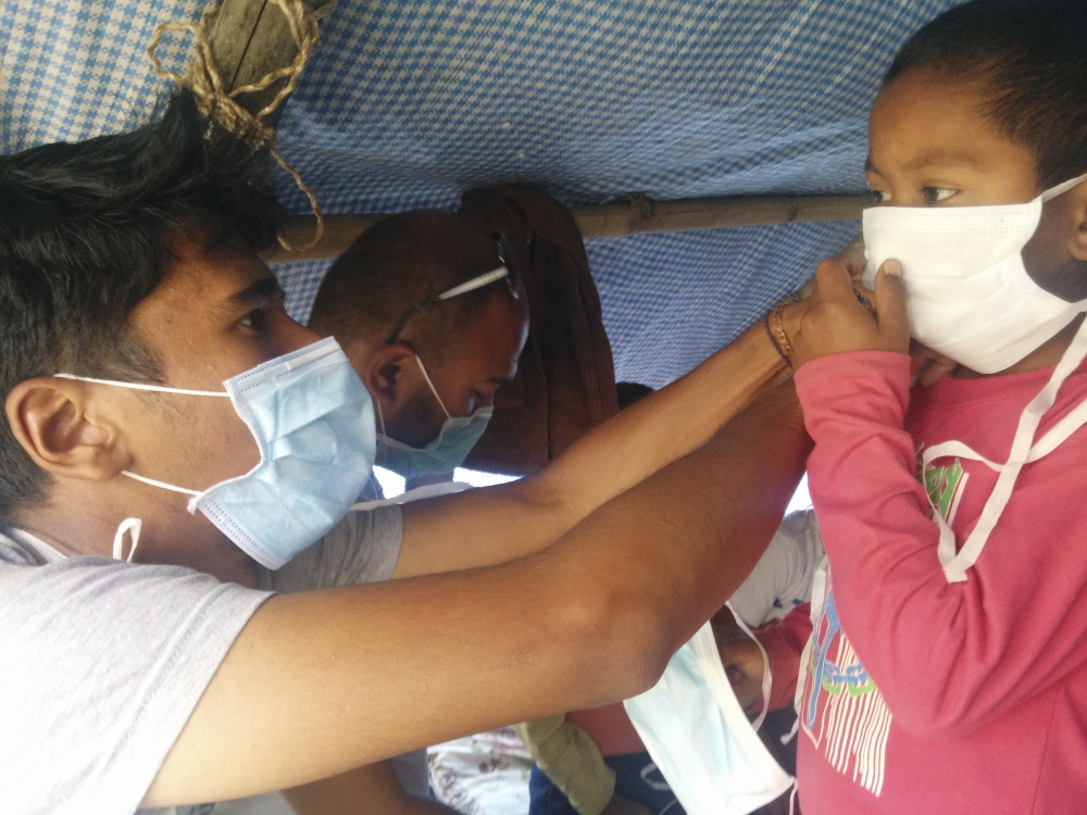 Surya Barki, left, a native of Nepal and a student at College of the Atlantic in Bar Harbor, assists a Nepalese child in securing a face mask in the village of Taudaha.