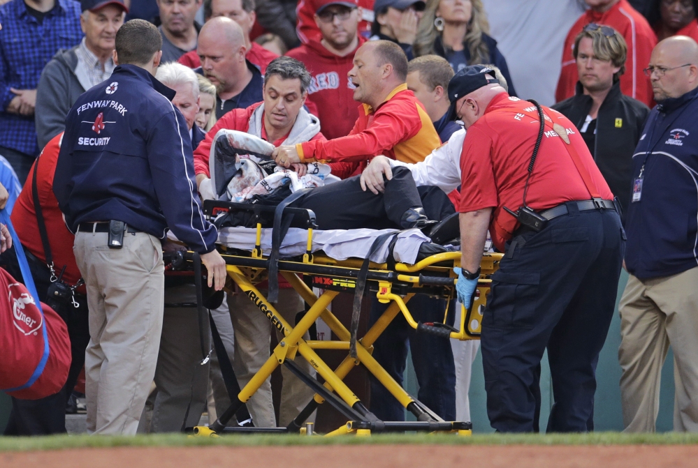 A fan, who was hit in the head with a broken bat by Oakland’s Brett Lawrie, is helped from the stands during Friday night’s game at Fenway Park.