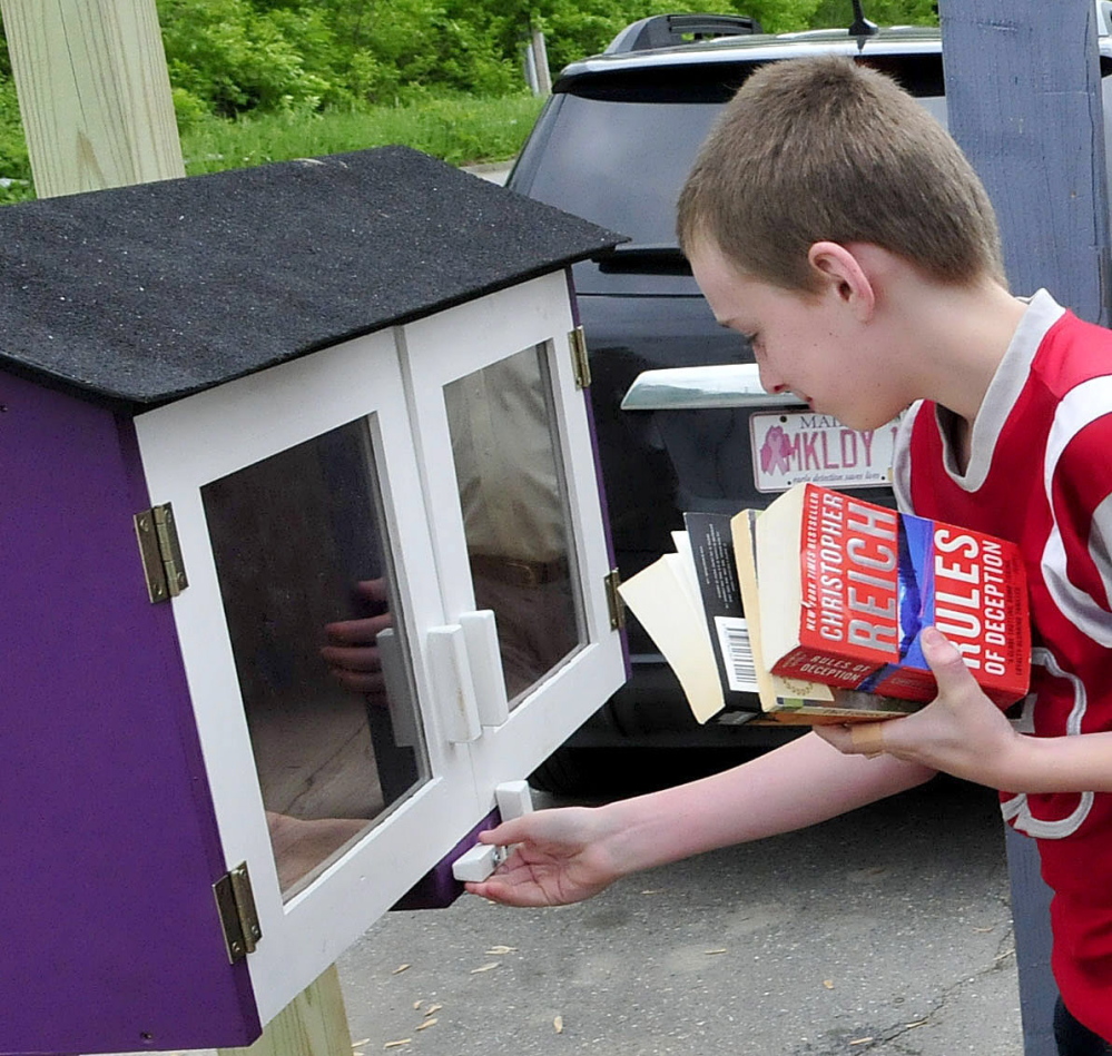 Holding an armload of books Wednesday, Logan O’Neal opens the doors of the Little Free Library near the South End Teen Center in Waterville.