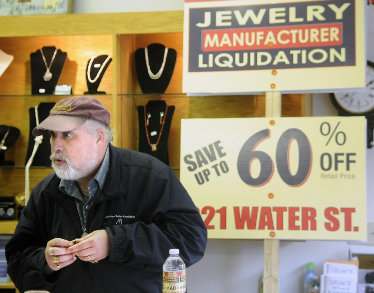 Daniel Lane appraises a ring last week at his Gardiner business, The Village Jeweler, in front of a sign that state officials told him to stop using to advertise a liquidation sale off-premises.