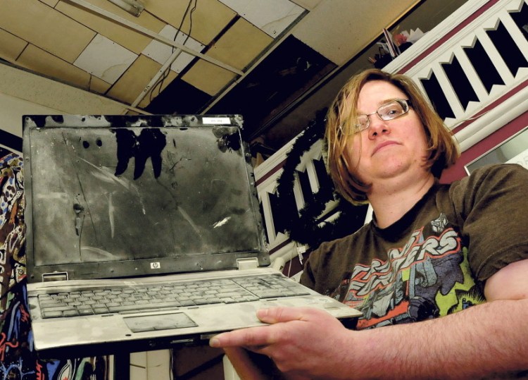 Amy Cyrway, co-owner of the Framemakers in Waterville, Monday holds a laptop computer that shorted out and caught fire after rain water flooded the store on May 28. There was substantial damage from the fire, and ceiling tiles, above, also collapsed. Employees covered the artwork inside.