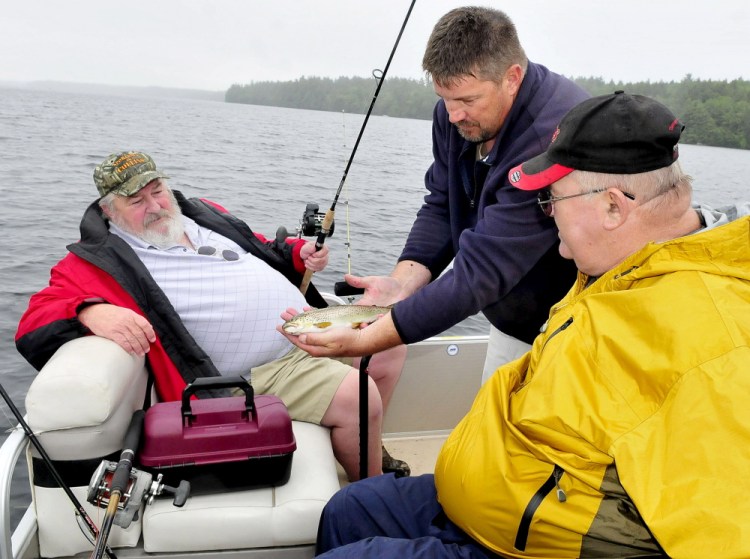 Volunteer boat captain Paul Stevens, of Belgrade, center, shows the brook trout that veteran Linwood Brayall, right, of West Gardiner, caught Tuesday on Great Pond in Belgrade. At left is veteran Carl Pettengill, of Farmingdale. The men took part in the Fishing Extravaganza, which provides an opportunity to relax and socialize with other veterans.