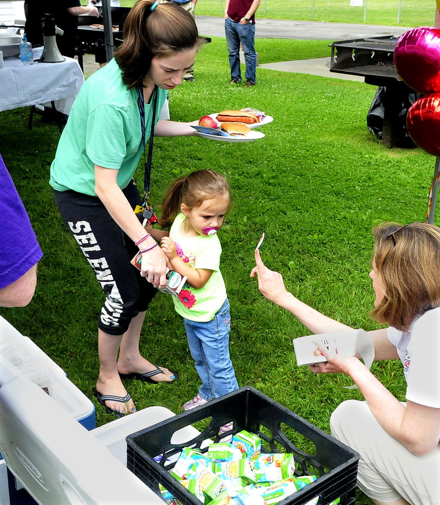Katie Hoffman of the Maine Dairy and Nutrition Council offers a sticker to McKenzie Reynolds and her mother, Nikida, during the Waterville kickoff of the AOS 92 and USDA summer food program on Monday.