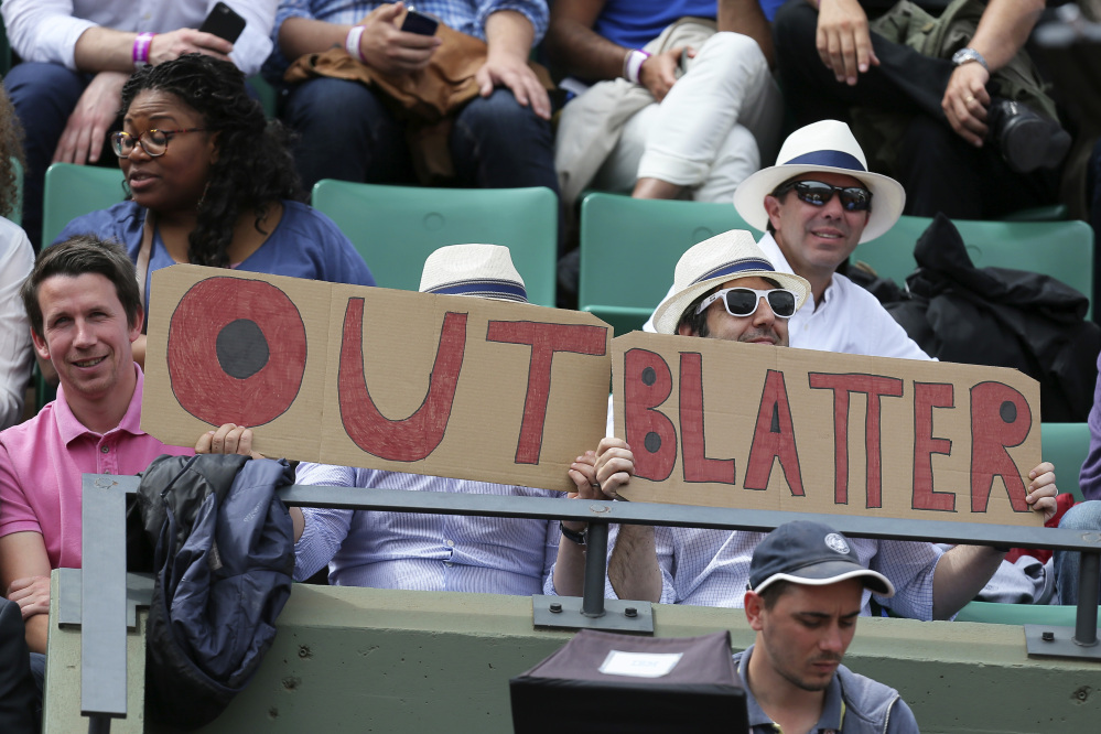 Spectators at the French Open tennis tournament hold signs Tuesday reading “Out Blatter,” referring to FIFA President Sepp Blatter, who said Tuesday that he will resign from his position in the midst of a corruption investigation.