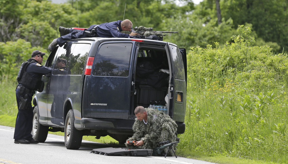 A law enforcement agent looks through a sniper scope while another in camouflage assembles a weapon during a search for two escaped killers in Boquet, N.Y., Tuesday.  