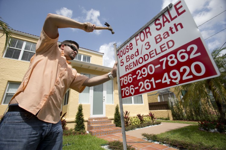 Robert Almirall, director of marketing and special assets coordinator for Mederos & Associates Real Estate Inc., puts up a sign in front of a home in Miami this spring.