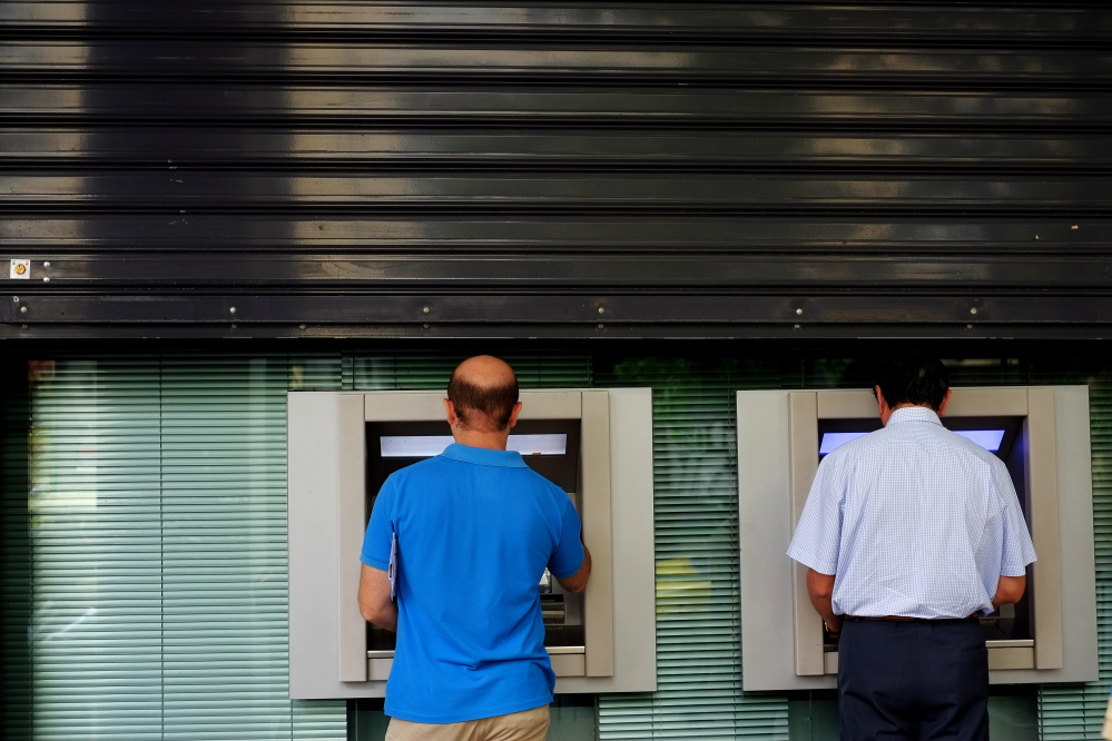 Men use the ATM outside of a closed bank five days before the upcoming referendum, in central Athens, on Tuesday.