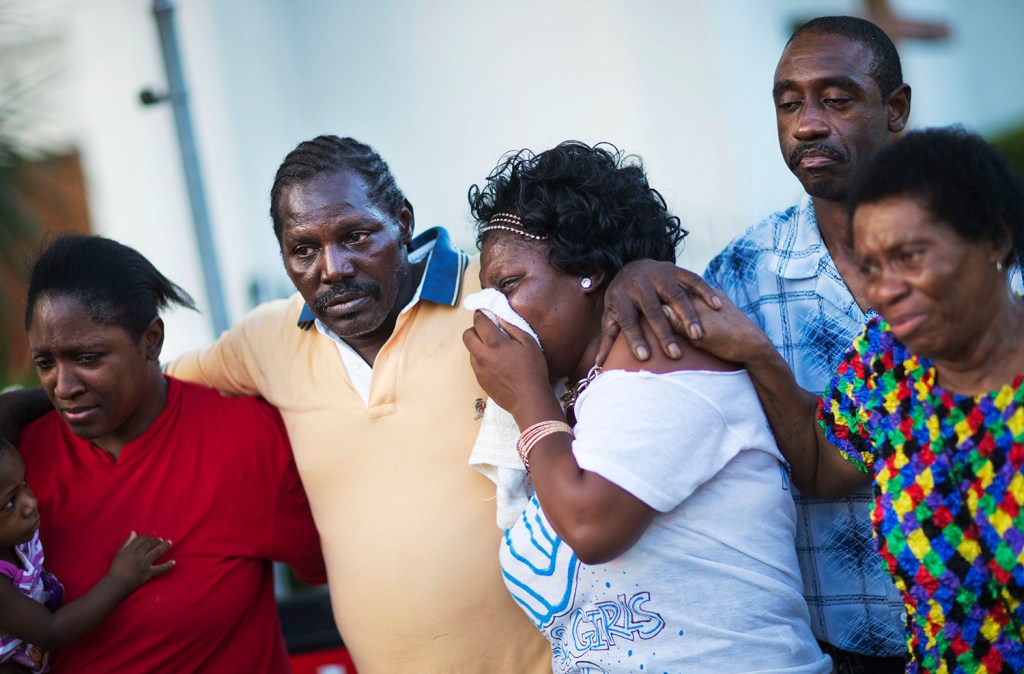 Gary and Aurelia Washington, center left and right, the son and granddaughter of Ethel Lance who died in Wednesday's shooting, leave a sidewalk memorial in front of Emanuel AME Church comforted by fellow family members.