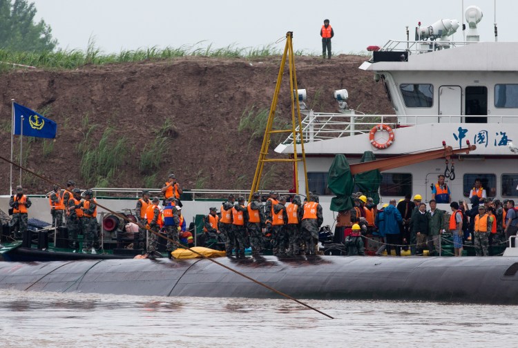 Chinese soldiers stand near a wrapped body as rescuers work on the capsized ship  on the Yangtze River. Hopes dimmed Wednesday for rescuing more than 400 people still trapped in the river cruise ship that overturned in stormy weather. The Associated Press