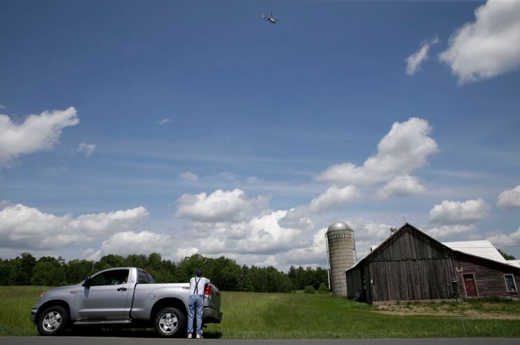 A man watches from the roadside as a law enforcement helicopter hovers over a wooded area near Dannemora, N.Y., Wednesday. The Associated Press