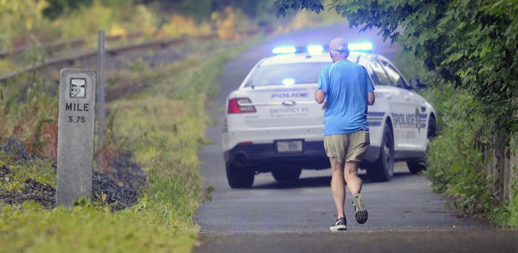 A jogger approaches a Gardiner police cruiser blocking the Kennebec River Rail Trail in Farmingdale on Friday morning. A body was discovered on the tracks behind the Farmingdale Town Office at dawn, according to State Police, who are investigating the death as a suicide.
