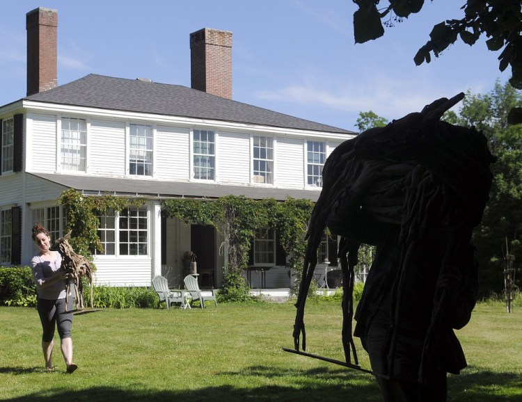 Arielle Cousens, left, and Benjamin Stoodley carry the two pieces of their sculpture “Navi” onto the lawn of the Vaughan Homestead on Friday in Hallowell. The Augusta artists installed the driftwood and welded sculpture ahead of a reception for several pieces on display at the homestead, a nonprofit arts and cultural institution.