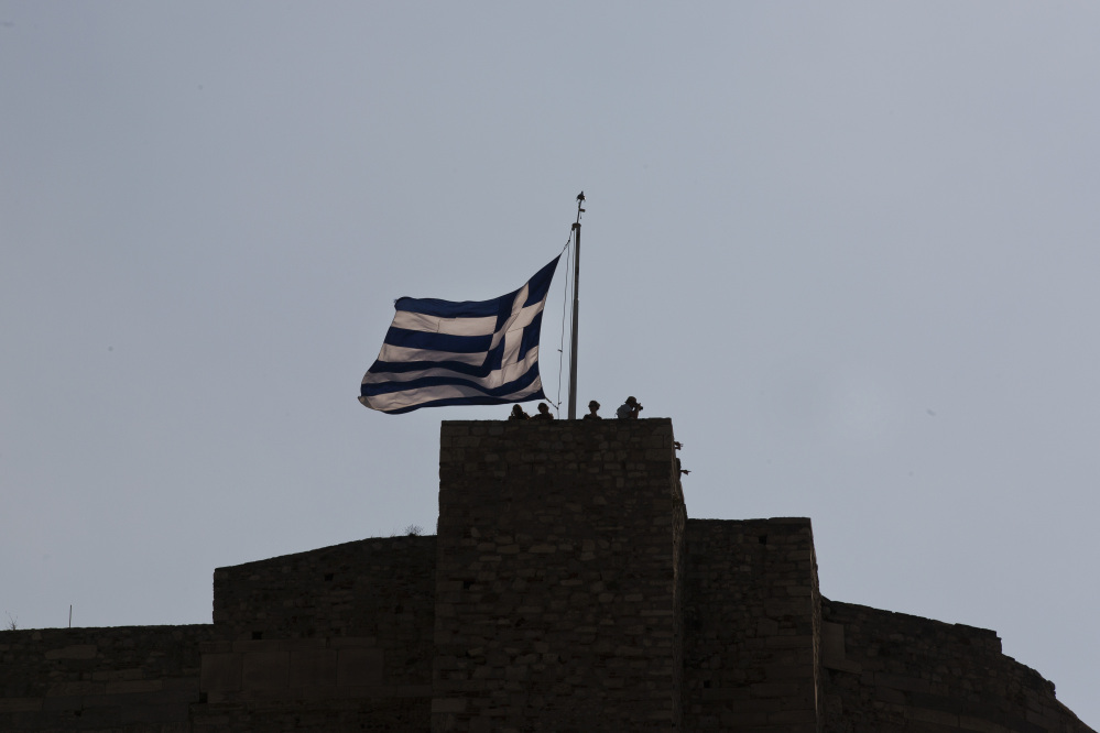 Tourist stand above a huge Greek flag at the top of the Acropolis hill in Athens, Saturday.