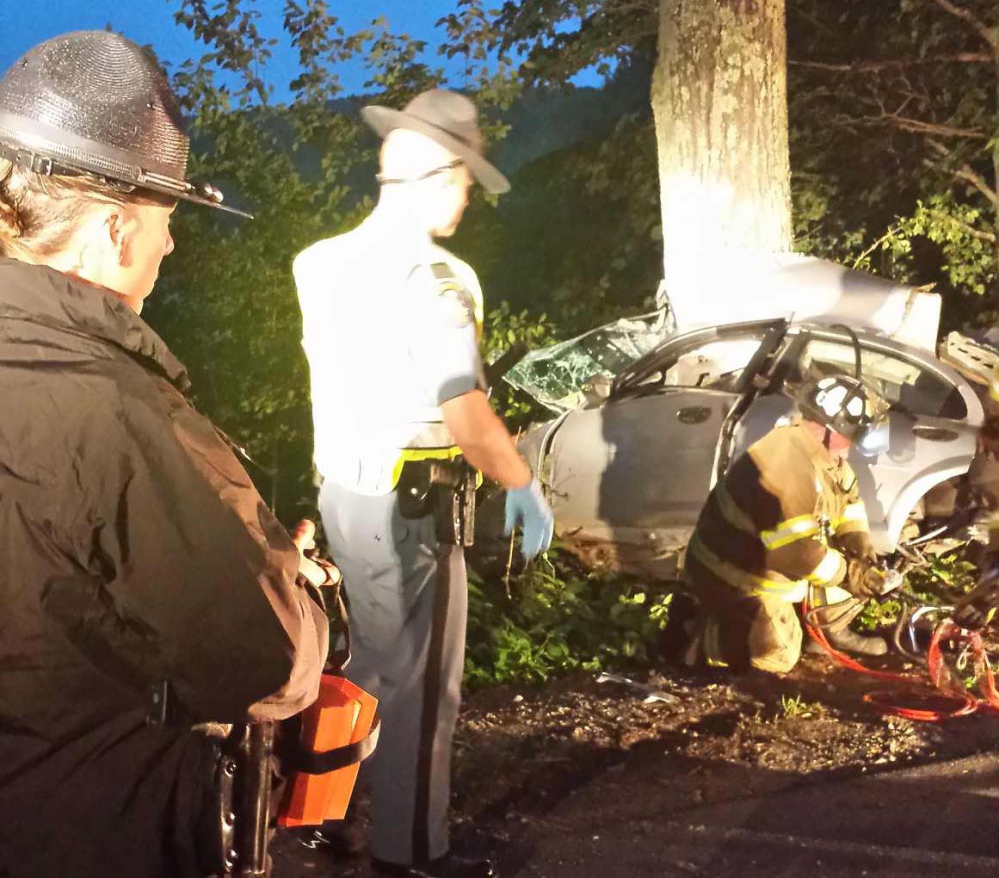 Troopers Diane Vance and G.J. Neagle watch as firefighters use extrication equipment to remove two dead bodies from the car after a crash early Saturday morning in Vassalboro.