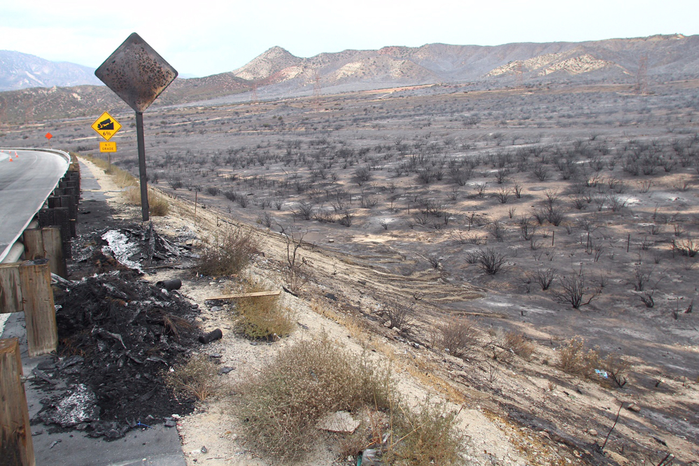 Burned terrain is seen on the reopened southbound side of Interstate 15, the main connector between Southern California and Las Vegas in the Cajon Pass, Calif., on Saturday, July 18, 2015. The fire swept across Interstate 15 on Friday, destroying the vehicles before burning three homes and 44 more vehicles in the community of Baldy Mesa. It has blackened 5.5 square miles. (AP Photo/Matt Hartman)