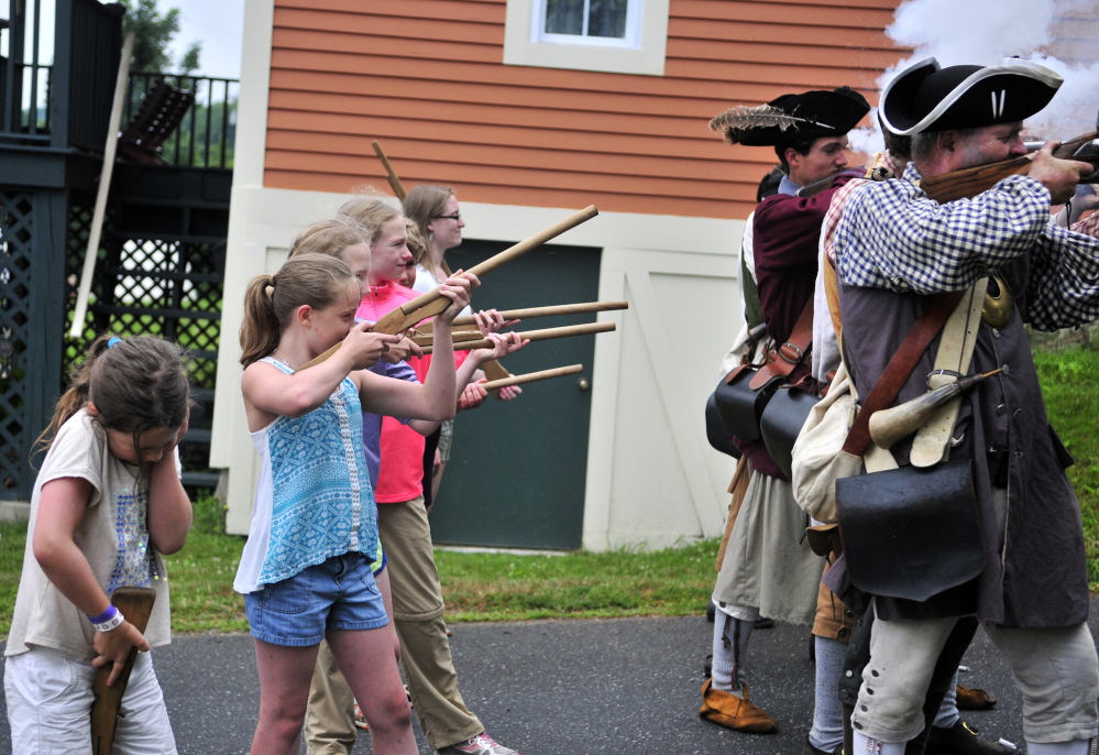 Emily Day, 9, of Auburn, left, lowers her wooden toy rifle to cover her ears as re-enactors fire a volley Saturday during an Old Fort Western encampment set up for the annual Old Hallowell Day celebration in Hallowell. Peter Morrissey, as Capt. James Howard, far right, led children in marching drills with firing around a field beside Hallowell Seafood.