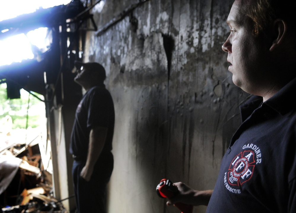 Gardiner firefighter Gary Hickey, left, and Fire Department Capt. Nate Sutherberg wait on Sunday in a doorway for colleagues to search the burned-out shell of 235 Water St. for missing equipment. The crew hoped to recover gear lost in the blaze that destroyed the structure last Thursday.