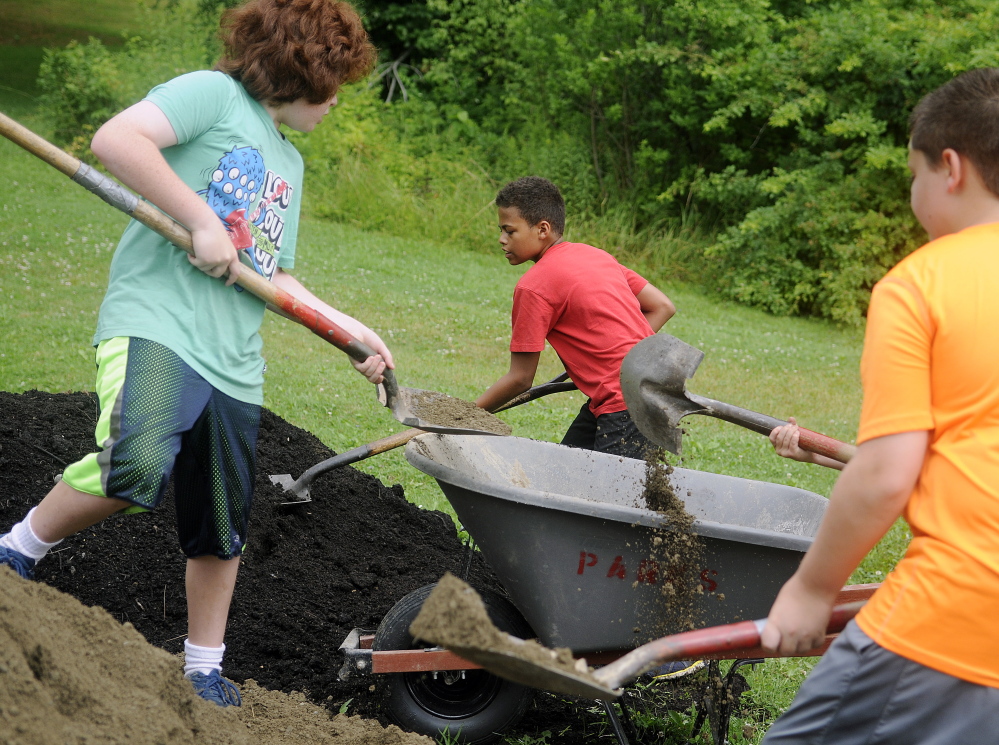 Children load a wheelbarrow with compost and soil Monday at the new garden beds erected at the Buker Community Center in Augusta.