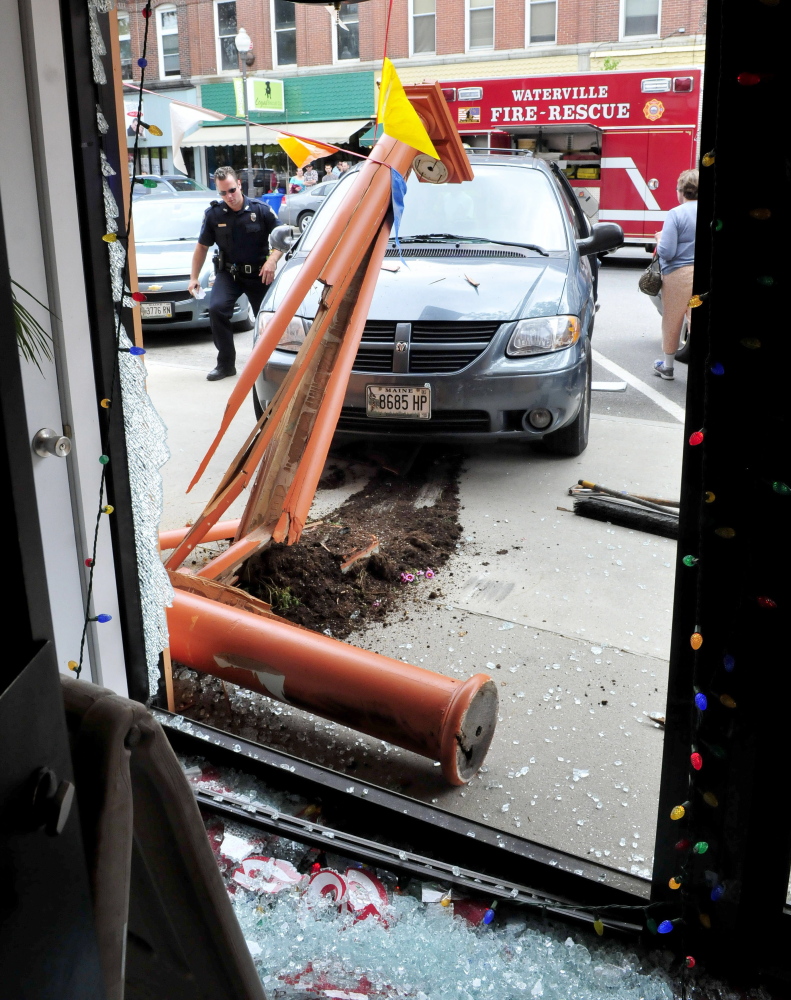Waterville police officer Damon Lefferts surveys the van that crashed into the front of the Jewel of India Restaurant on Main street in Waterville on Thursday. No one appeared injured and the front glass door and a wood structure were destroyed.